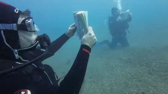 Su altında kitap okuyan dalgıçlar